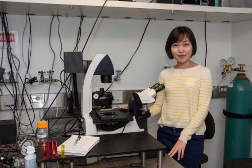 Suin Shim standing in a lab by a microscope.