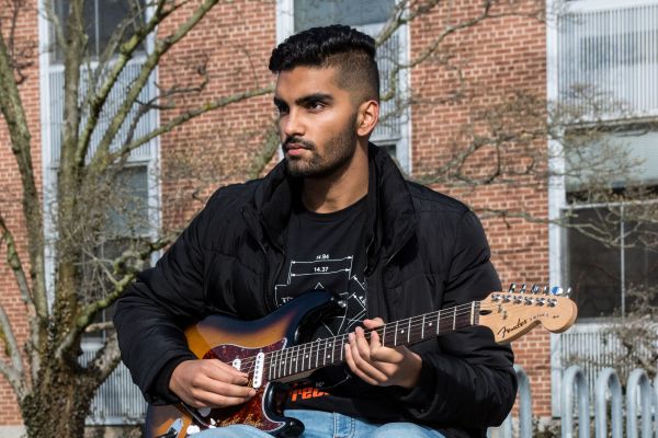 Ritvik Agnihotri sitting on a stone wall playing a guitar.