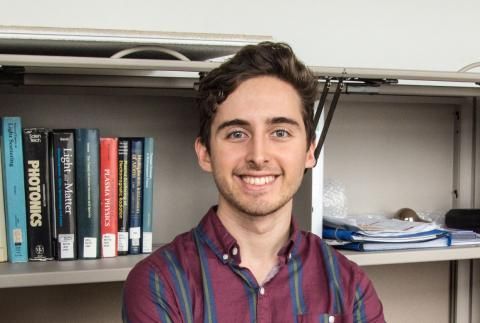 Christopher Galea smiling in front of shelf with books and papers