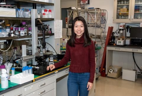 Estella Yu smiling by lab equipment