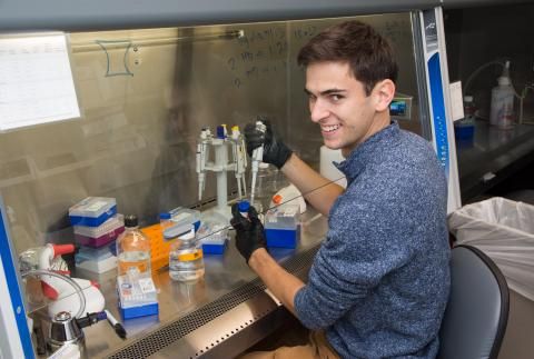 Matthew Heinrich with pipette behind shield in lab