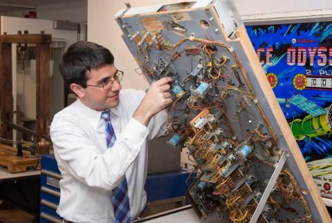 Larry Loprete in shirt and tie lifting top of Space Odyssey pinball game to show inner workings 