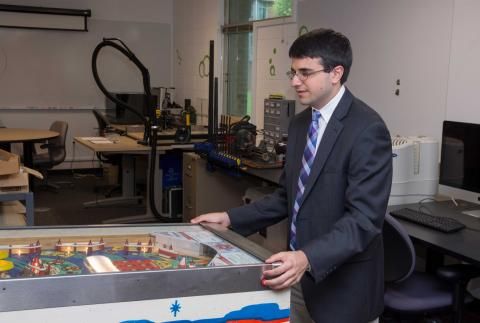 Larry Loprete dressed in suit and tie playing pin ball game