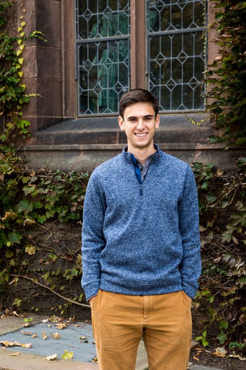 Matthew Heinrich standing in front of a a building covered in ivy on campus.