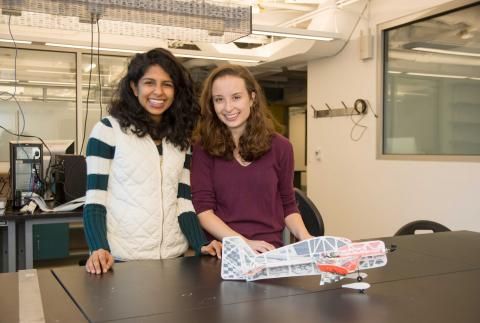 Soumya Sudhakar and Grace Lynch smile while standing by model airplane in lab