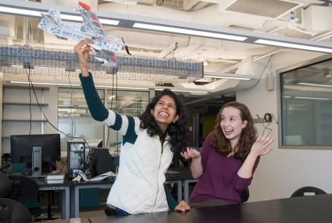 Soumya Sudhakar and Grace Lynch smile as Soumya holds model airplane up in the air