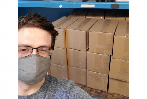 Person with face mask and glasses standing near stack of boxes