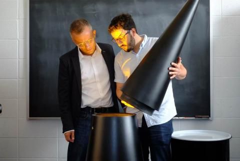 Alexander Glaser and Sébastien Philippe in front of chalkboard are illuminated by yellow glow as they look into model warhead
