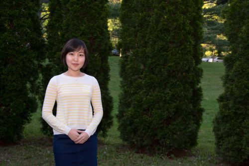 Suin Shim standing outside in front of a row evergreen trees.