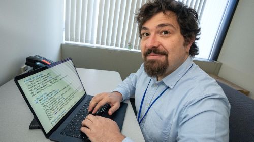 Egeman Koleman writing code on his laptop, looking at camera