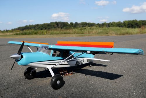 A model airplane with flaps raised sits on the runway.