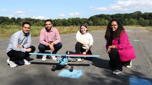 Four researchers crouch on a tarmac next to an RC plane fitted with plastic flaps.