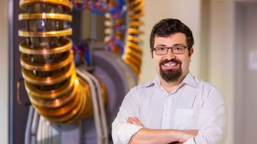 Egemen Kolemen smiling in front of a model fusion reactor.