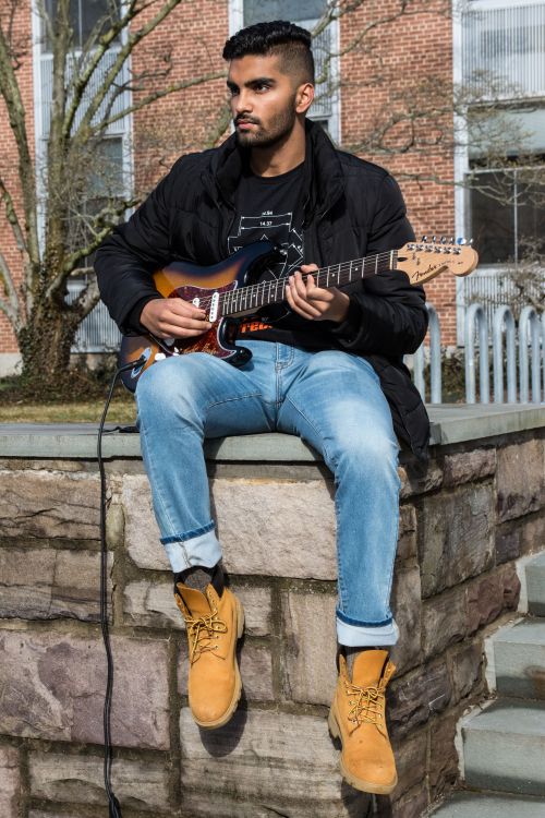 Ritvik Agnihotri sitting on a stone wall playing a guitar.