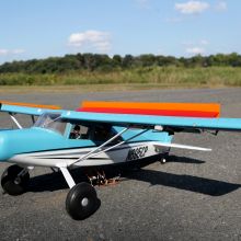 A model airplane with flaps raised sits on the runway.