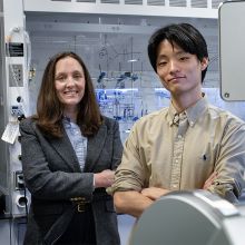 A woman and a man stand side by side in front of a laboratory fume hood.